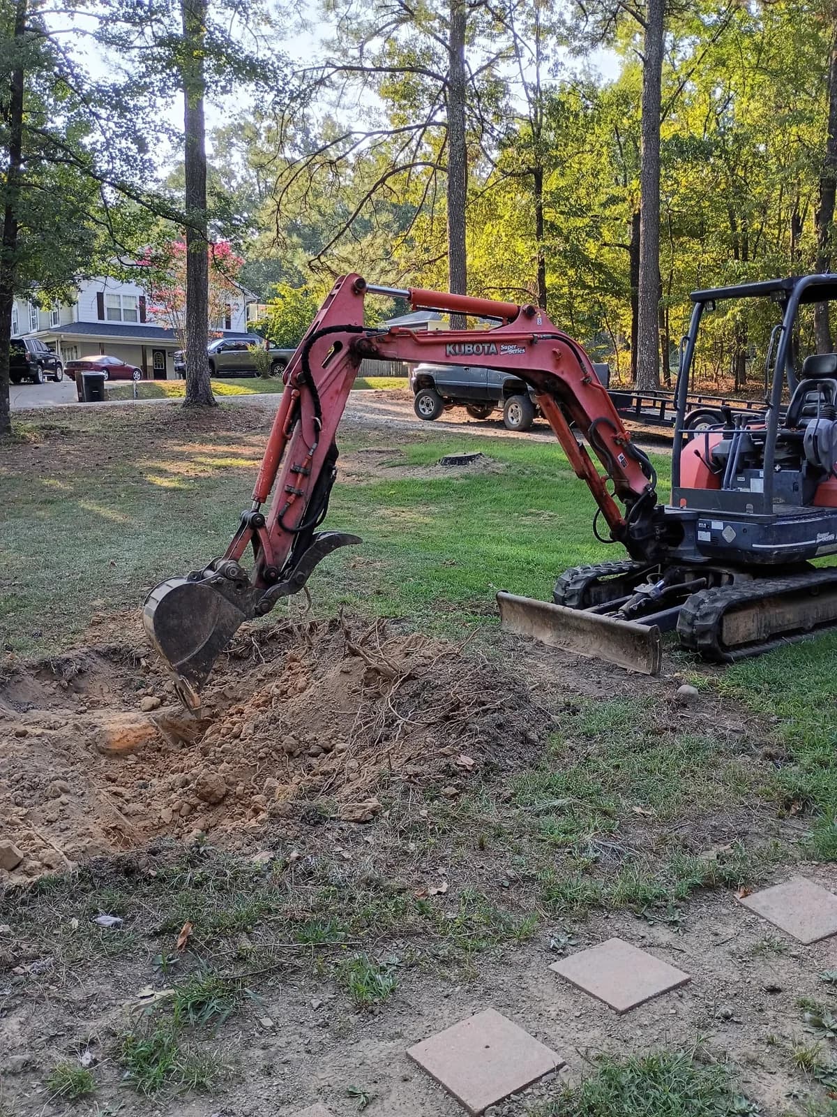 Red Dirt mini excavator digging and loosening roots during property dirt work