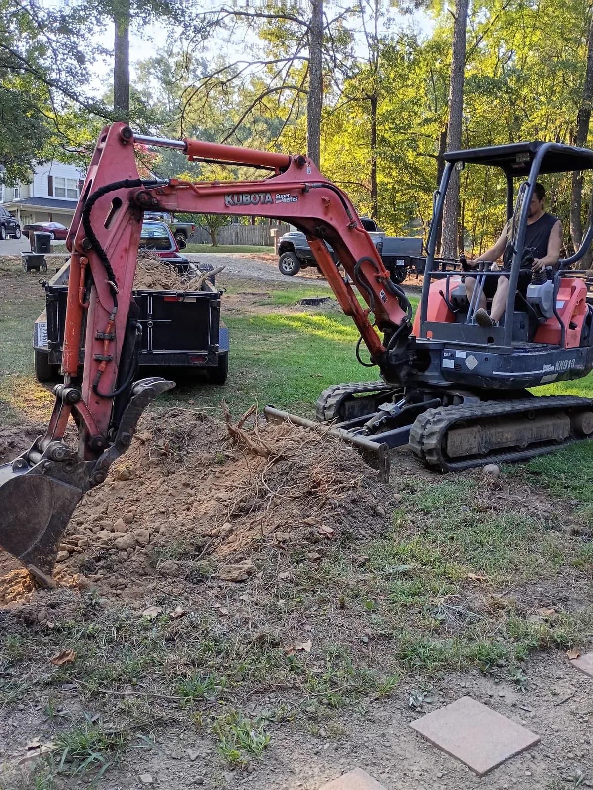 Mini excavator beside a dump trailer during a local cleanup and dirt-work job