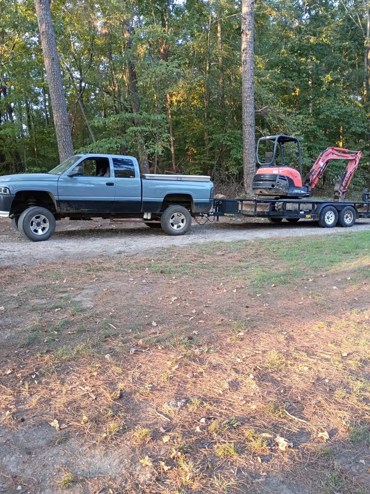 Red Dirt pickup hauling a mini excavator on a flatbed trailer