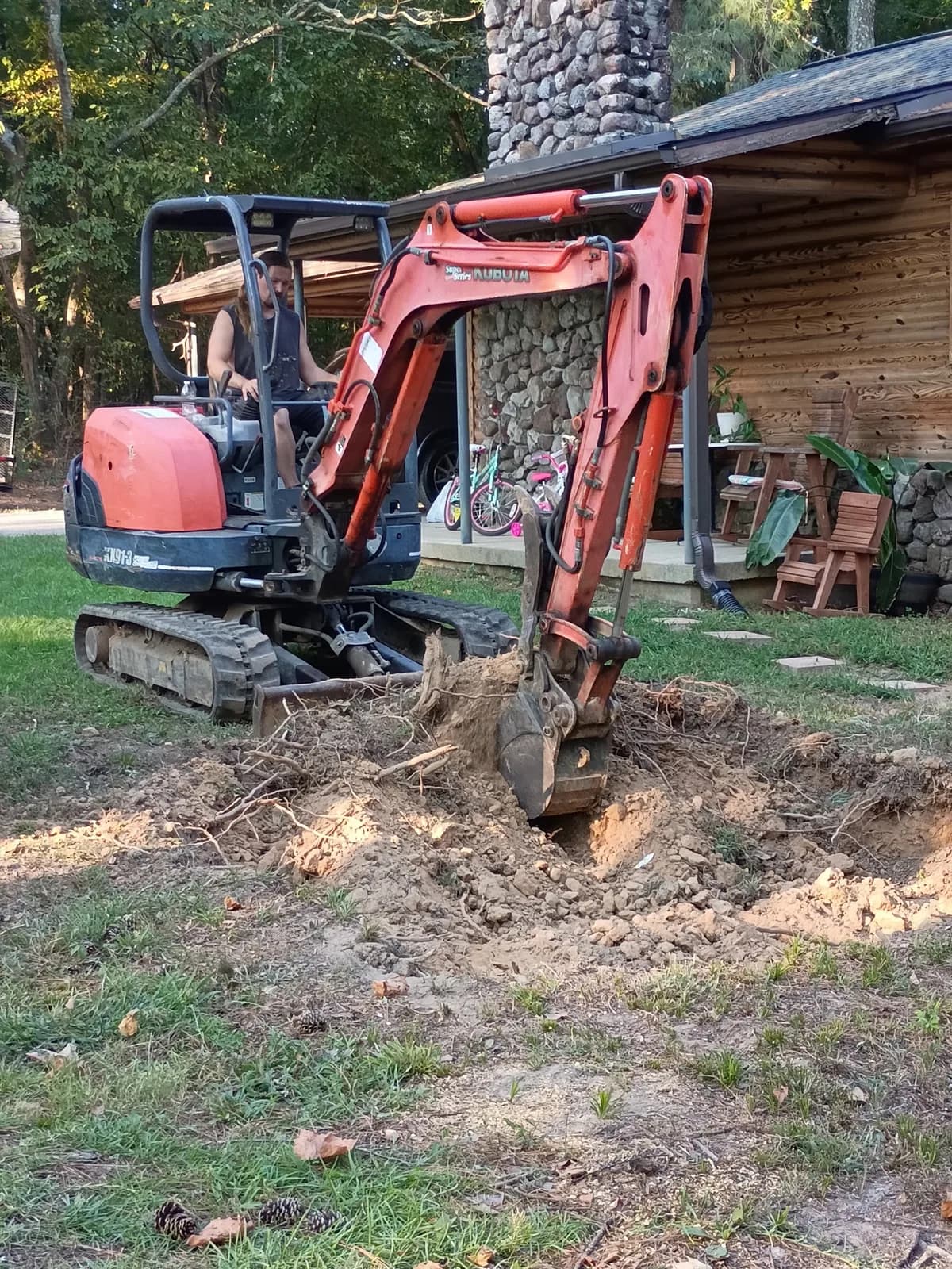 Mini excavator removing roots and stump material near a residence